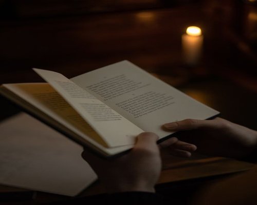 A person holding a physical book under soft, diffused reading light